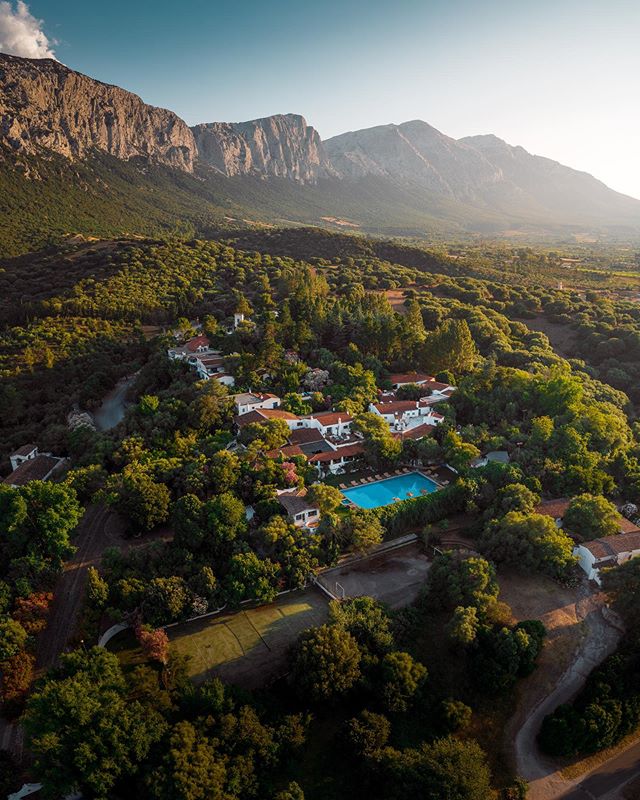 Su Gologone’s buildings and pool among trees beneath the Supramonte mountains